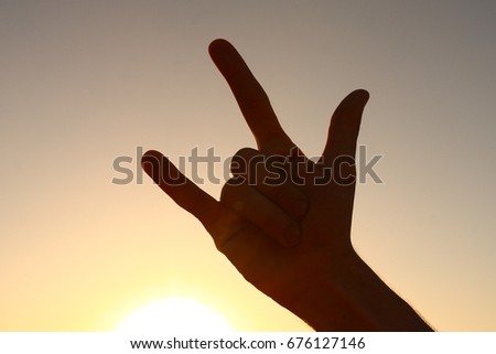 Hand giving the devil horns gesture. Sunset background, hand silhouette