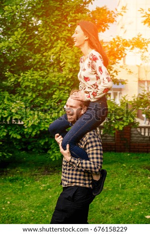 Happy young beautiful couple in sunlight fooling around in the park. Girl with long hair and white shirt with flowers. Guy in plaid shirt, beard and pigtail