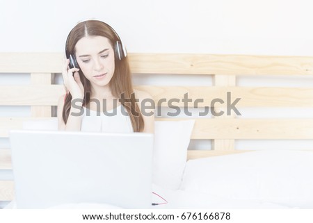 Portrait of beautiful caucasian woman in morning listening music by laptop sitting on bed at home