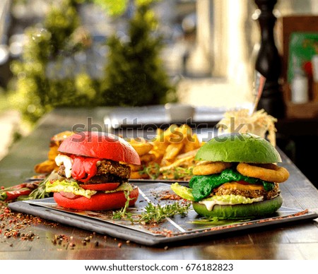 Red and green hamburgers with French fries on the table.