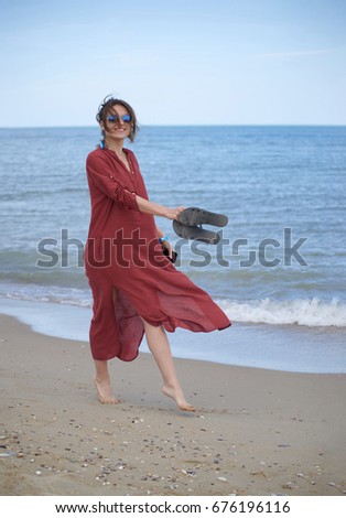 Beautiful women in red beach dress on seashore. Walking on a beach. With Empty space for text and can be used for vacation or travel or may be tourism commercial about resting not far from the sea