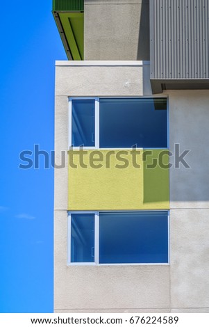 A minimalist architectural building has a yellow rectangle between two window on separate floors. The building stands next to a beautiful blue sky. 