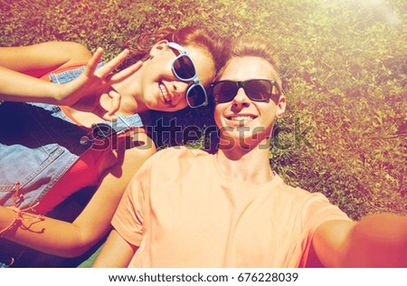 love and people concept - happy teenage couple in sunglasses lying on grass and taking selfie at summer