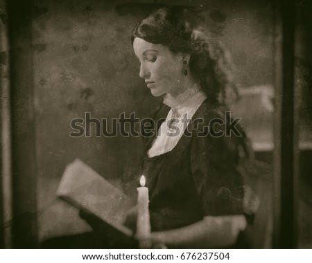 Worn wet plate photo of victorian girl reading book by candlelight behind window.