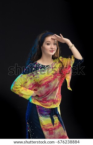 Girl with long hair in multi-colored suit for belly dancing in baladi style dancing and posing on black background