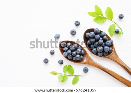 Fresh  blueberries in a wooden spoons on a white surface of a table. Closeup, top view.