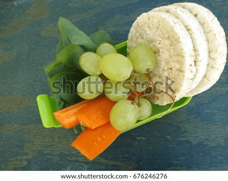 School lunch boxing. Plastic container, rice crackers and vegetables. Spinach, carrots and grapes.