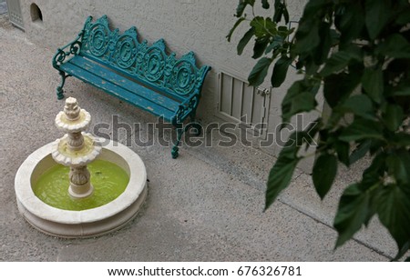 Green metal bench in front of a small fountain, seen from above