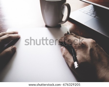 Picture of paper, pencil, laptop, coffee cup and men hand on wooden table. selective focus, soft tone