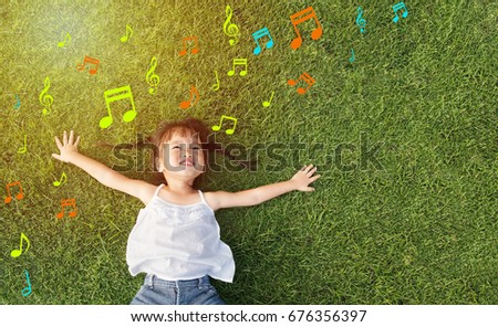 Asian little girl smile and lay on grass with music note background Royalty-Free Stock Photo #676356397