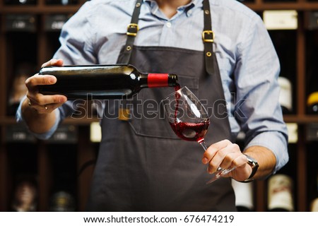 Male sommelier pouring red wine into long-stemmed wineglasses. Royalty-Free Stock Photo #676474219