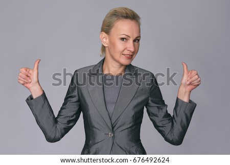 Confident middle aged businesswoman giving the thumbs up against a gray background