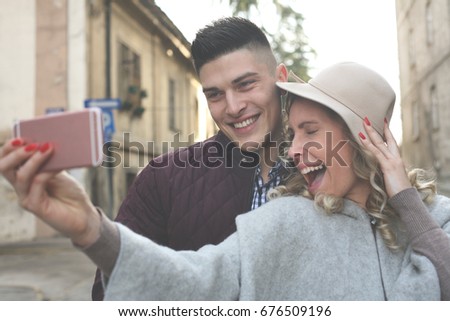 Happy couple standing on street an taking self-picture with smart phone.