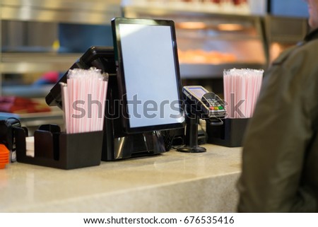Cash and order desk with order screen and card payment terminal with cashiers on back  in fast food restaurant