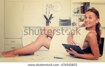 Cheerful woman lying on desk with cardboard with documents in company office indoors