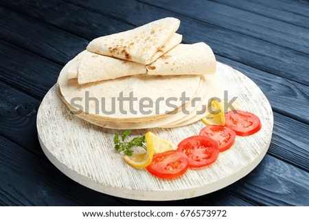 Round board with yummy tortillas and sliced tomato on wooden table