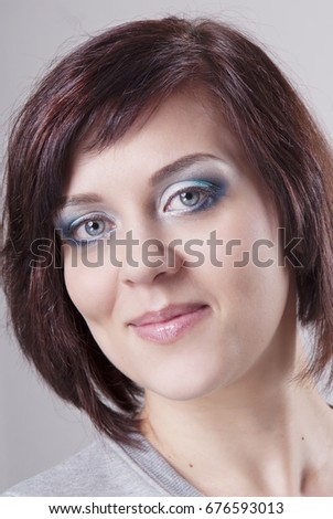 Brunette girl with clean skin, hair basic bob  and cocktail makeup. Isolated grey background. A light smile.
