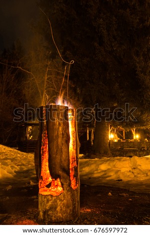Massive wooden log on fire, with sparks, at fire camp in the mountains; night time
