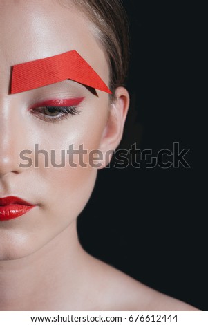 portrait of fashionable woman with red lips and paper eyebrow posing for fashion shoot isolated on black