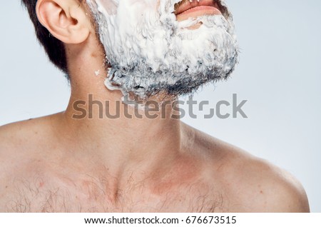 Young guy with beard on white isolated background in foam for shaving.