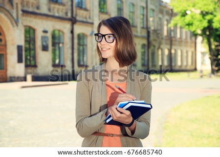 Woman student. Young female student in glasses with books standing near university.