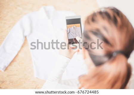Young women taking photo to shirts with cell telephone or smartphone digital camera for Post to sell Online on the Internet . moving to packing for selling online business  internet of things concept