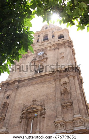 Old church tower in murcia in spain made from beige stone with unfocused leaves framing the picture and the morning sun coming through