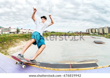 Teenager skater in a cap and shorts on rails on a skateboard in a skate park