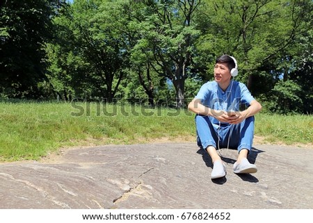 man sitting on stone while looking up and listening to music on headphones 