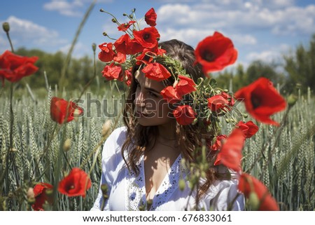 Young summer girl with poppies in her hair in a white dress in the nature.