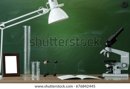 Teacher or student desk table. Education background. Education concept. Microscope, copybook, beakers and photo frame on the table. Chemistry or biology lesson.
