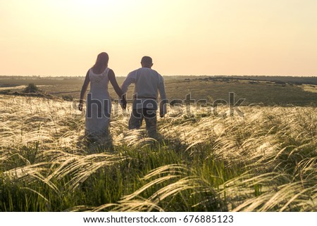 Happy couple man and woman in national Slavic clothes walking in field on sunset and holding hands. Welcome to Russia