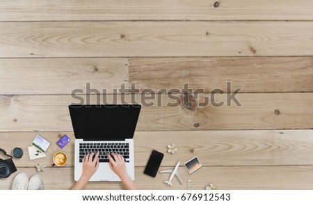 Top view man's hands using smartphone and laptop with coffee cup, Airplane, Photos and Credit card on  wooden table at office.
