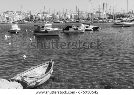 Yachts docked at the port of Malta. Boats moored in a row on the background of modern city. A shabby old boat among the luxury ships. Black and white picture