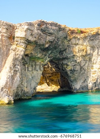 Picture is showing rocky coast landscape. On picture there is a cave or better say stone window and a green sea showed on the picture. 