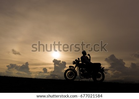Motorcycle or motorbike Silhouette with male rider is smoking and standing at the river.