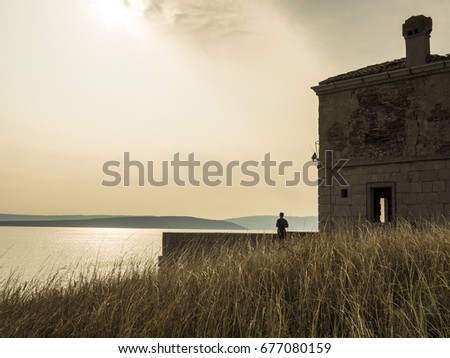 Silhouette of a person looking onto the sea next to a abandoned lighthouse.