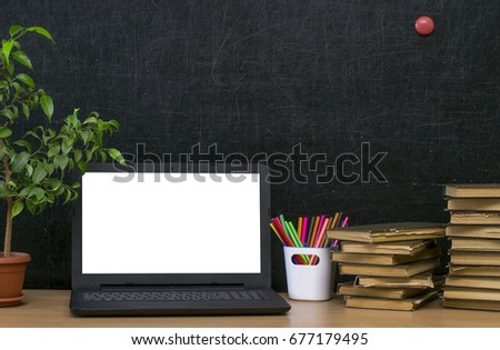 Teacher or student desk table. Education background. Education mockup concept. Laptop with blank screen, green plant tree, stacked books and colour pencils on blackboard (chalkboard) background.