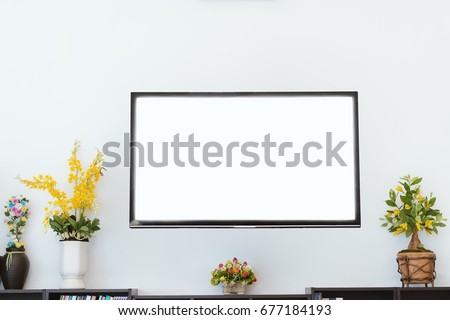 The white screen TV on the room wall with flower vase on wooden cabinet.The room is decorated with plastic flower pots.Modern TV on the white room wall for a variety of applications.