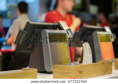 Cash and order desk with order screen and card payment terminal with cashiers on back  in fast food restaurant