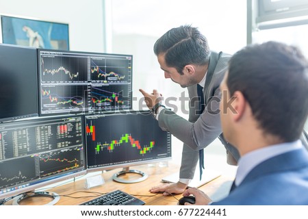 Businessmen trading stocks online. Stock brokers looking at graphs, indexes and numbers on multiple computer screens. Colleagues in discussion in traders office. Business success concept. Royalty-Free Stock Photo #677224441
