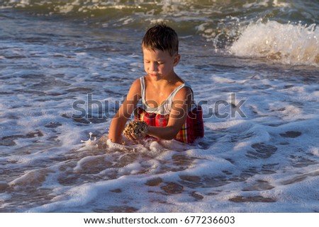 Little boy playing with sand and sitting in sea surf at vacation