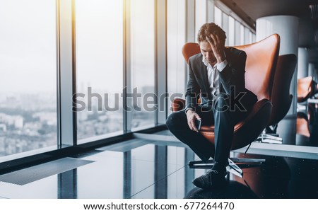 Businessman in formal suit is sitting on orange armchair and holding his head in depression after phone call about his company went bankrupt with copy space for text, your logo or advertising message Royalty-Free Stock Photo #677264470