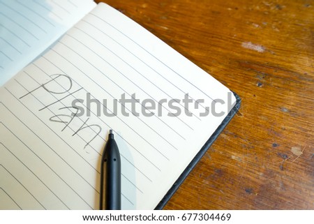 hand writing "Plan" on notebook with pencil on wooden table.