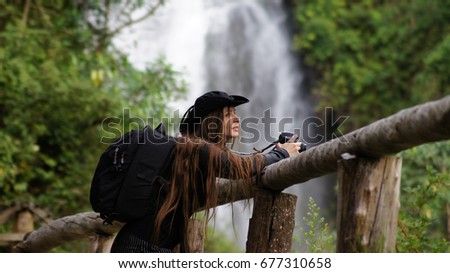 Female tourist with backpack shoots photos near Peguche waterfall, Otavalo, Ecuador.