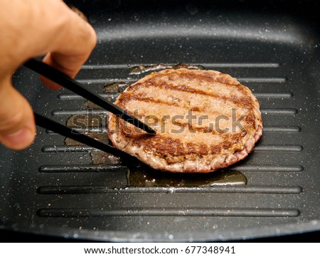 Hand turning delicious raw beef meat burger in a frying pan on cooking surface in kitchen