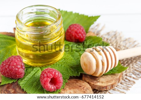 The bowl with honey, berries and leaves of raspberry on a wooden stand. Spoon with honey.
