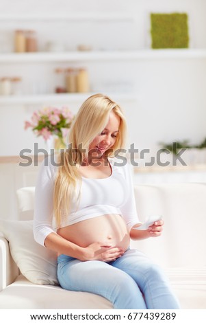 happy pregnant woman with ultrasound picture of her future baby, sitting on sofa at home