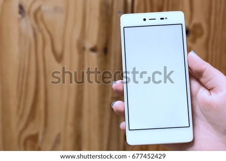Girl hand shows mobile smartphone in vertical position,blank screen,wooden background.