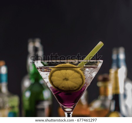 Colorful drink on the background of bottles in original shapes, cocktail drink with ice cubes, party night